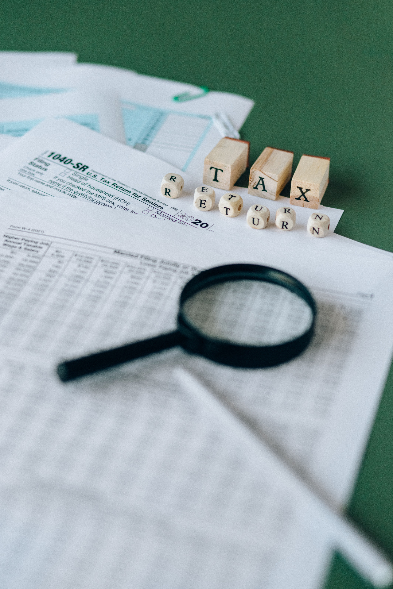 Tax documents and forms being reviewed with a magnifying glass.